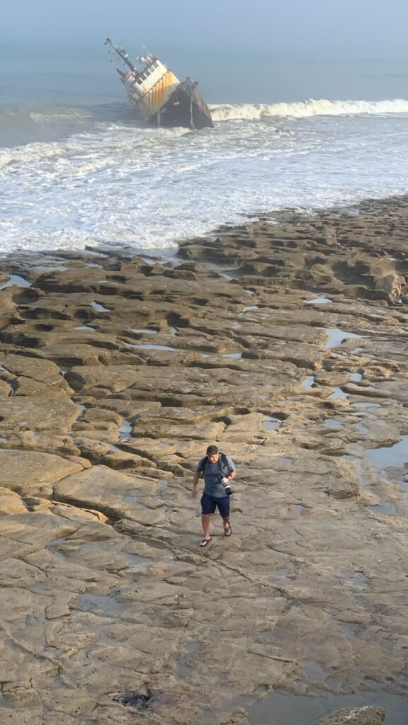 Photographer walking on the reef with shipwreck on the back